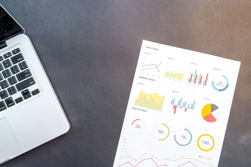 Laptop beside printed sales charts on a desk
